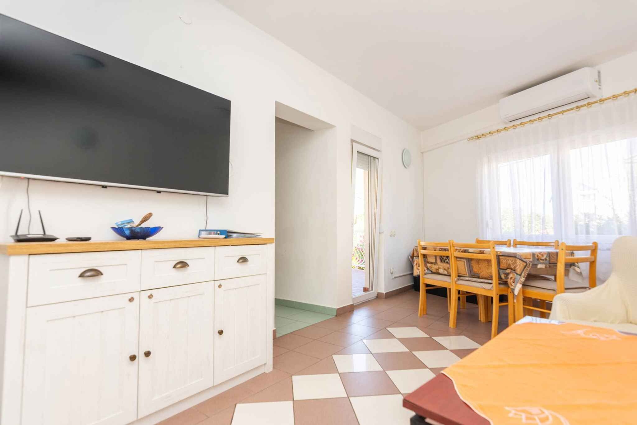 A room with a flat-screen TV, a dining table with chairs, a sofa, and a window with curtains.