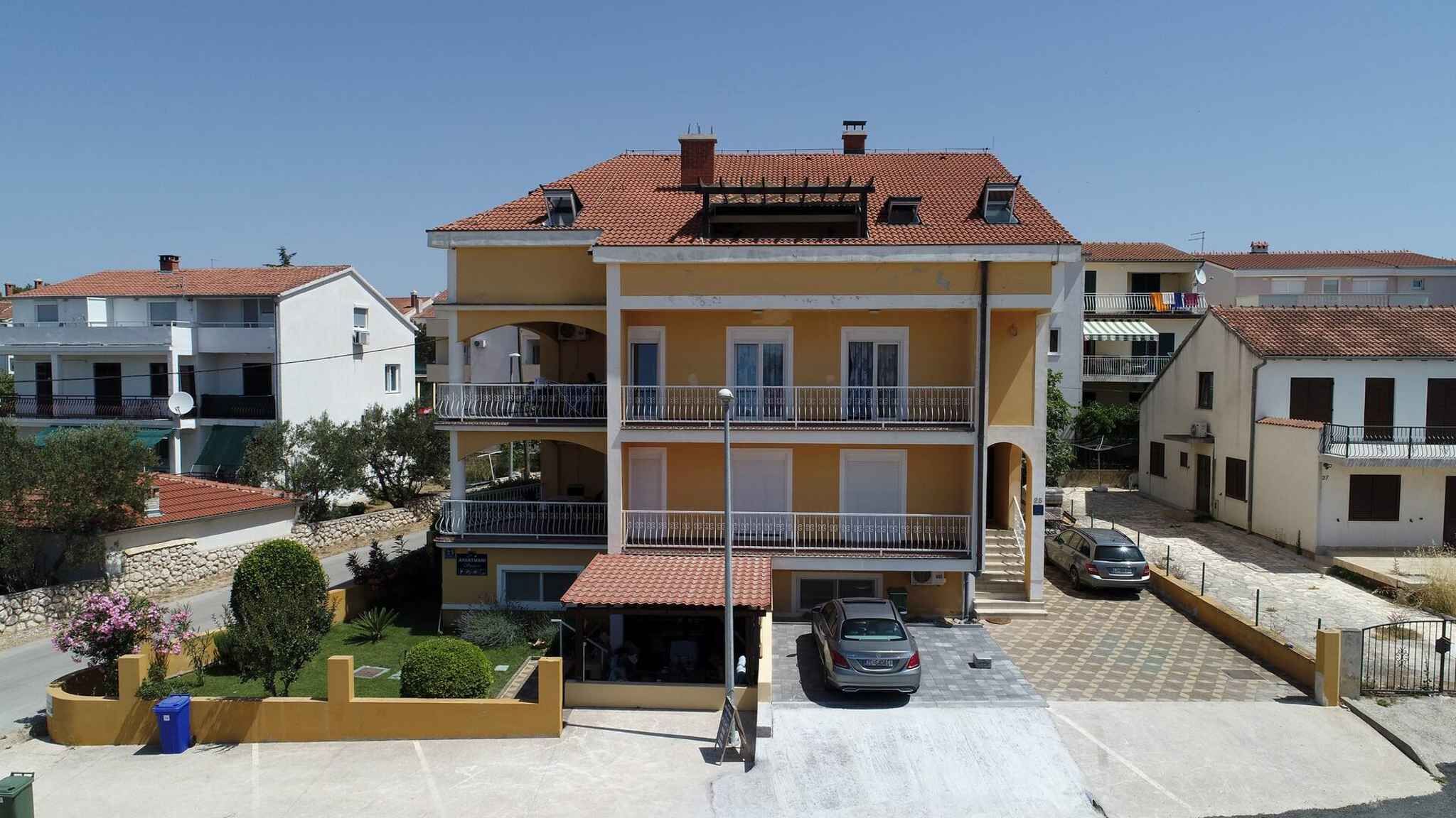 A multi-story residential building with balconies, a parking area, and a small garden.