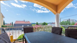 Un espacio de estar al aire libre cubierto, con una mesa y sillas, que ofrece vistas a un barrio residencial con casas y vegetación.