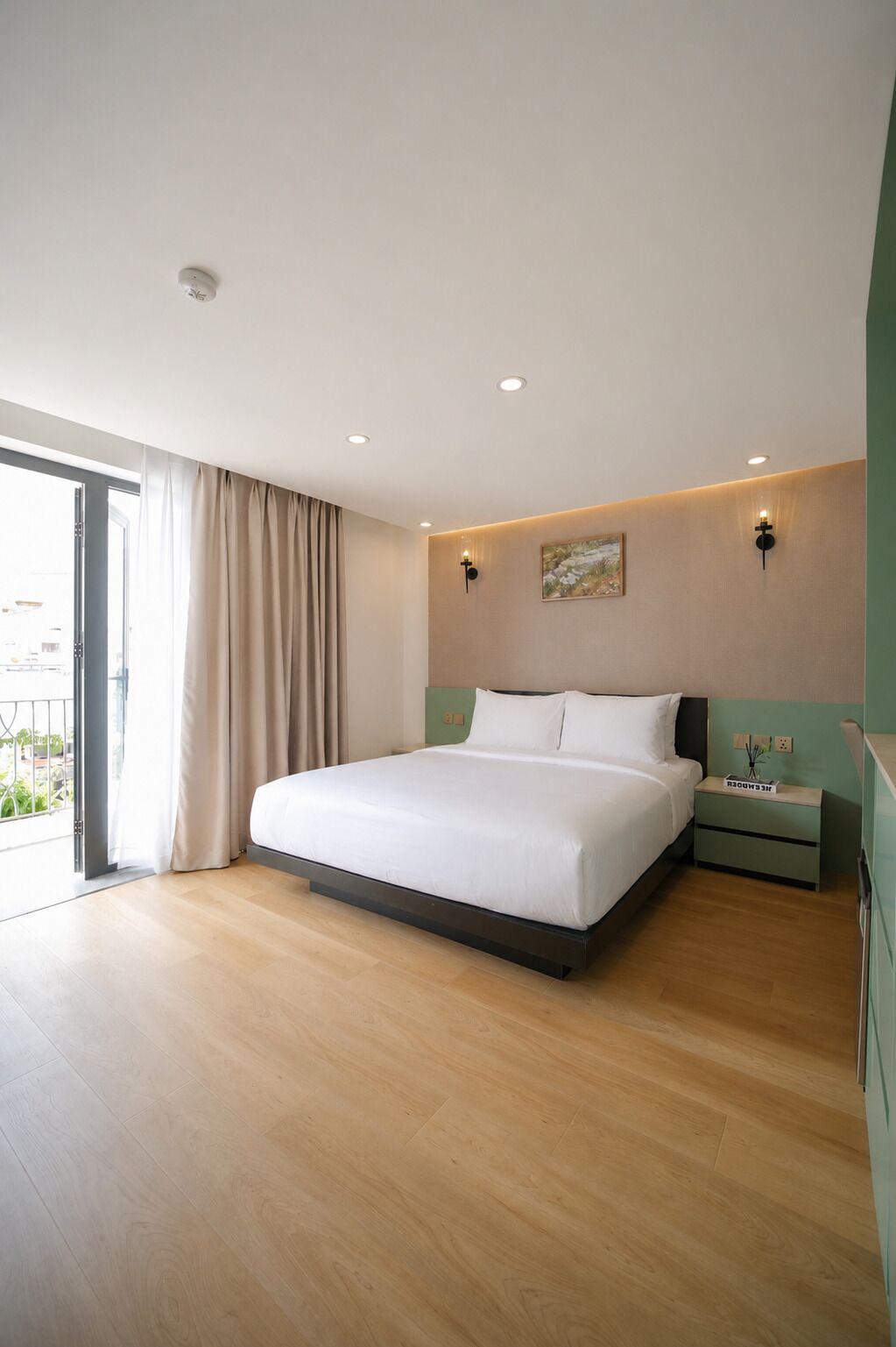 A modern hotel room with a large bed, a nightstand, a wall-mounted light, and a view through a sliding door.