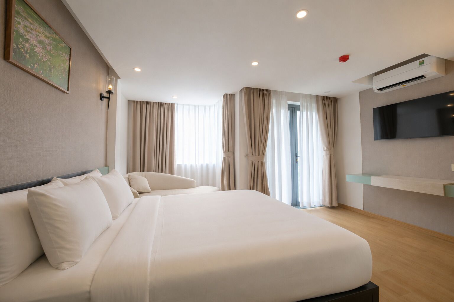 A hotel room with a large bed, a flat-screen TV, an air conditioning unit, and a window with curtains.