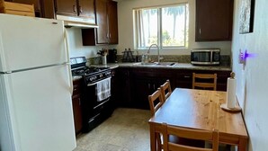 A compact kitchen with a refrigerator, stove, microwave, and wooden dining table. - Sunset Studio Retreat (Los Angeles)