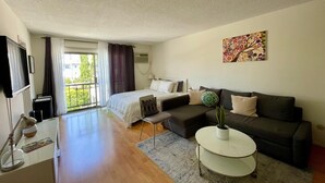 A modern hotel room with a bed, sofa, desk, and a balcony with curtains. - Sunset Studio Retreat (Los Angeles)