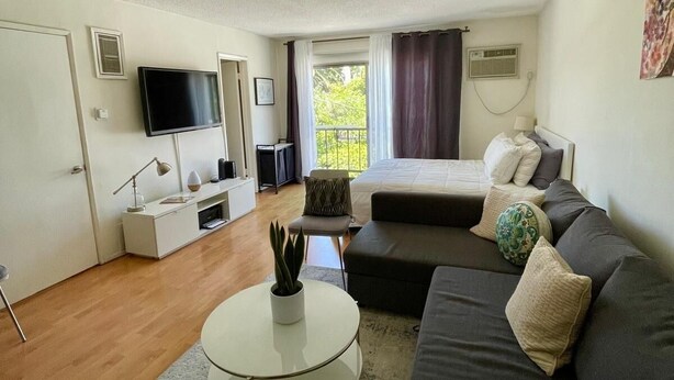 A modern living room with a sofa, a coffee table, a TV, and a balcony view. - Sunset Studio Retreat (Los Angeles)