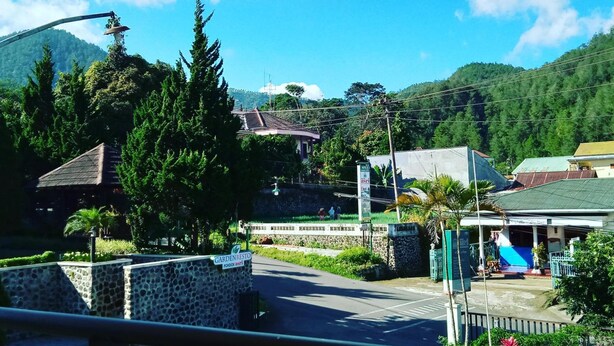 A hotel with a stone wall entrance, a covered outdoor area, and a view of mountains in the background. - Hotel Pondok Asri Tawangmangu (Tawangmangu)