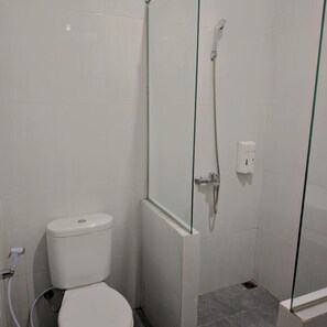 A small, white-tiled bathroom with a toilet, a glass shower enclosure, and a visible electrical outlet. - Hotel Pondok Asri Tawangmangu (Tawangmangu)