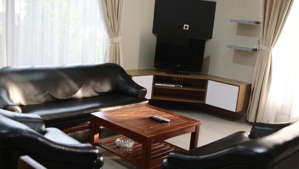 A living room with a black leather sofa, a wooden coffee table, and a television on a stand. - Hotel Pondok Asri Tawangmangu (Tawangmangu)