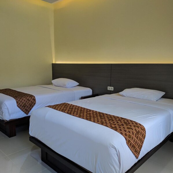 A hotel room with two beds, each with white linens and a patterned throw blanket.