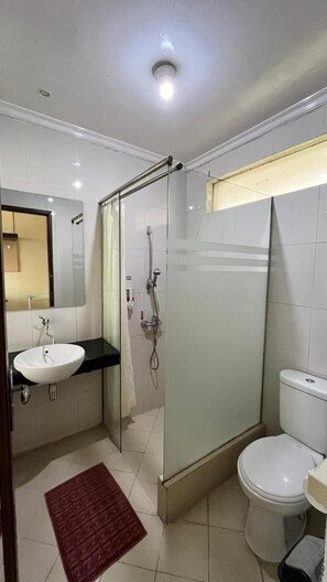 A bathroom with a glass-enclosed shower, a white sink, and a toilet. - Hotel Pondok Asri Tawangmangu (Tawangmangu)