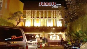La façade de l'hôtel Sunrise Jombor, avec son panneau bien visible, les voitures garées et un petit espace extérieur aménagé avec des sièges.