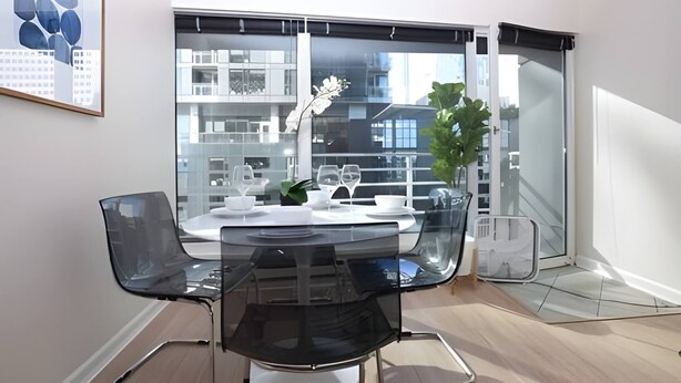 Een moderne eetruimte met een glazen tafel, zwarte stoelen en een uitzicht op gebouwen door grote ramen.