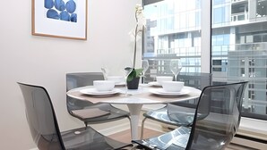 Een moderne eetruimte met een ronde tafel, transparante stoelen en een stadszicht door grote ramen.
