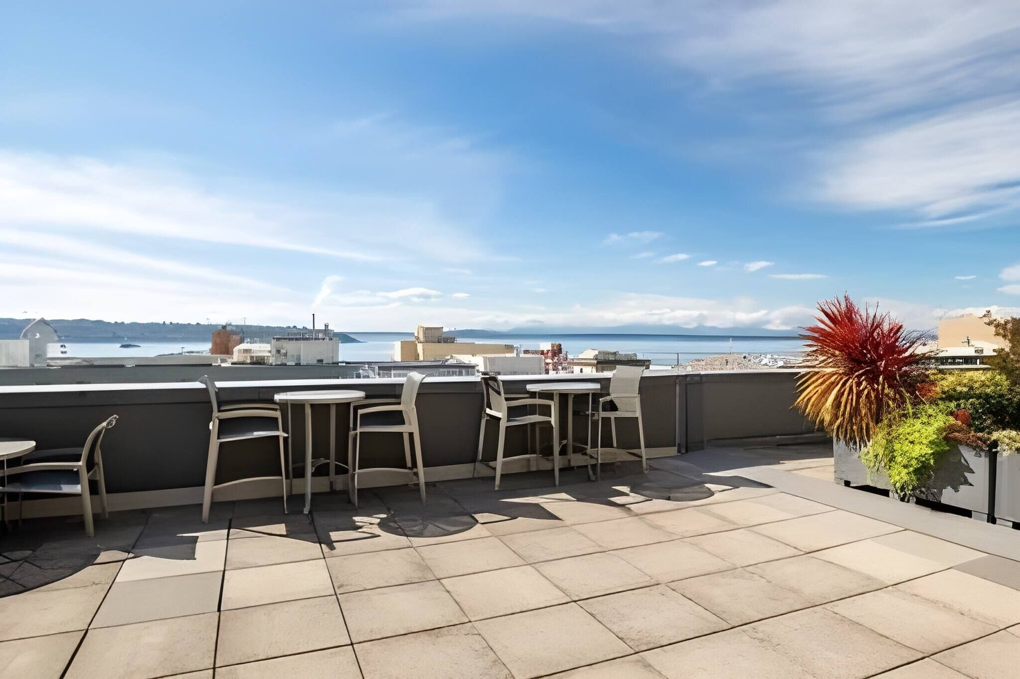 A rooftop terrace with outdoor seating, a view of the sea, and a potted plant.