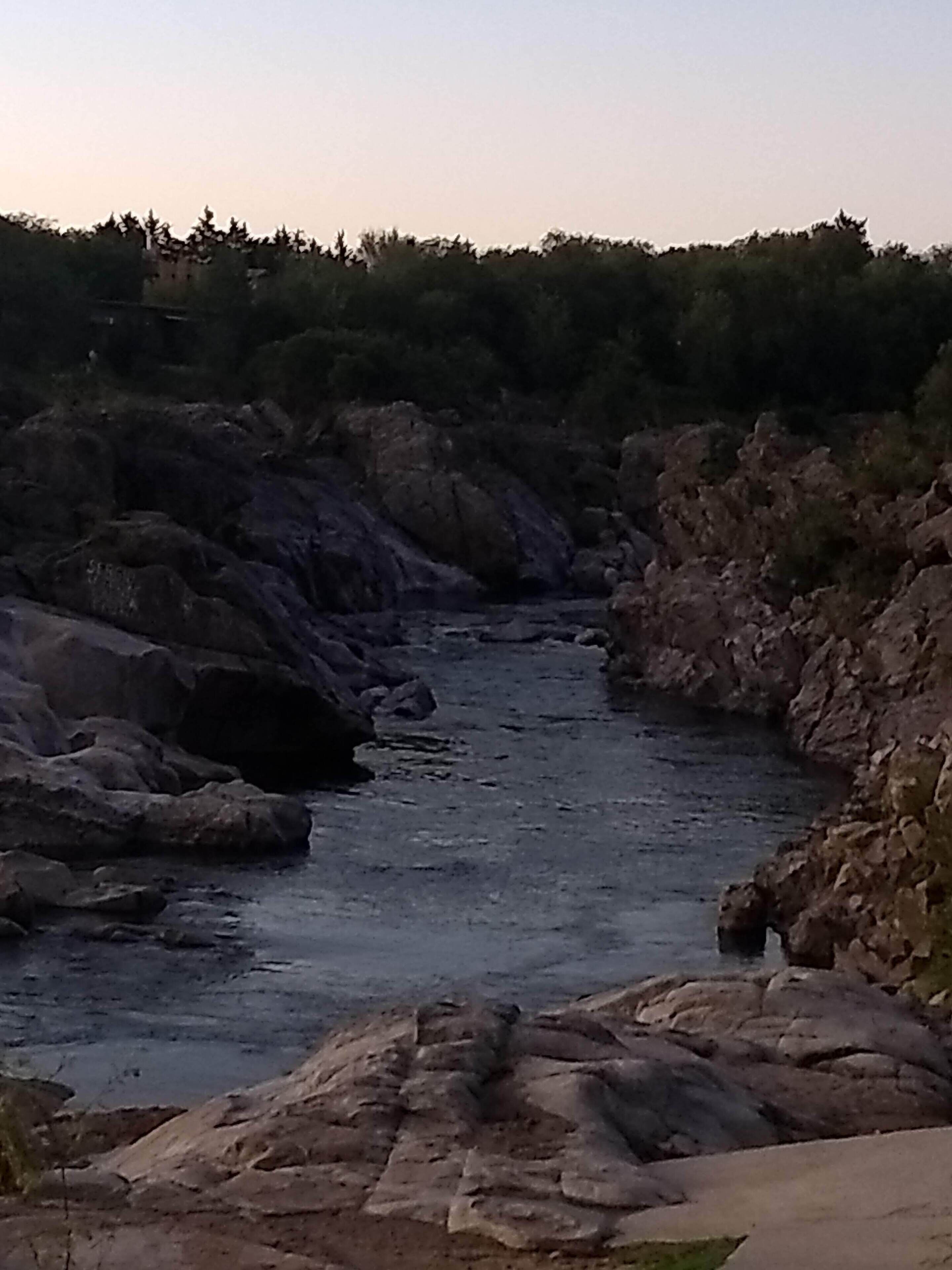 Ein Fluss fließt durch eine felsige Landschaft, im Hintergrund sind Bäume zu sehen.