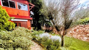 Un chemin de jardin mène à un bâtiment rouge orné d’antennes paraboliques, entouré d’une végétation luxuriante et d’un mur de pierre.
