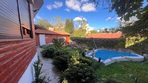 Un bâtiment en briques avec une piscine, entouré de verdure et bordé d’un chemin en pierre.