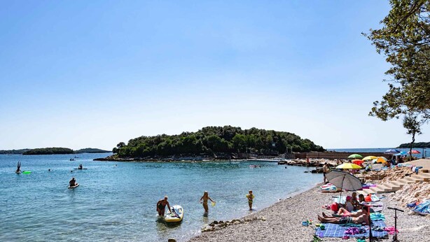 A beach with people swimming, a boat, and umbrellas. - Holiday home with Wi-Fi and air conditioning (Funtana)