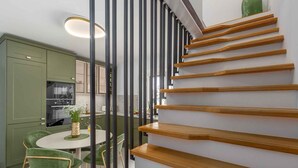 A modern kitchen with green cabinets, a dining area with a round table and green chairs, and a wooden staircase with a green vase on the top landing. - Holiday home with Wi-Fi and air conditioning (Funtana)