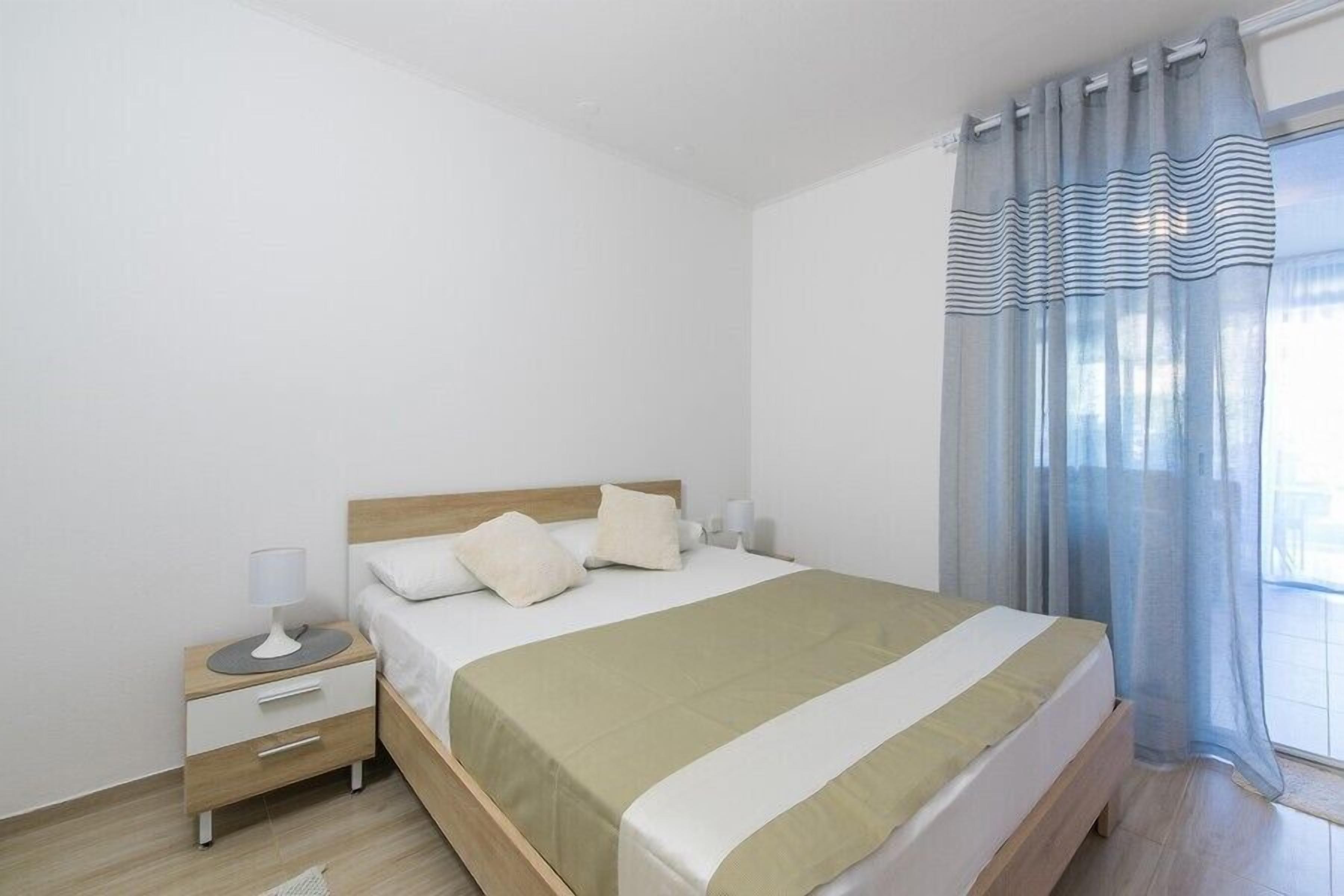 Een slaapkamer met een bed, nachtkastje, lamp en gordijnen.