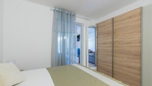 Ett sovrum med en säng, en garderob i trä, en skjutdörr i glas och utsikt över en balkong.