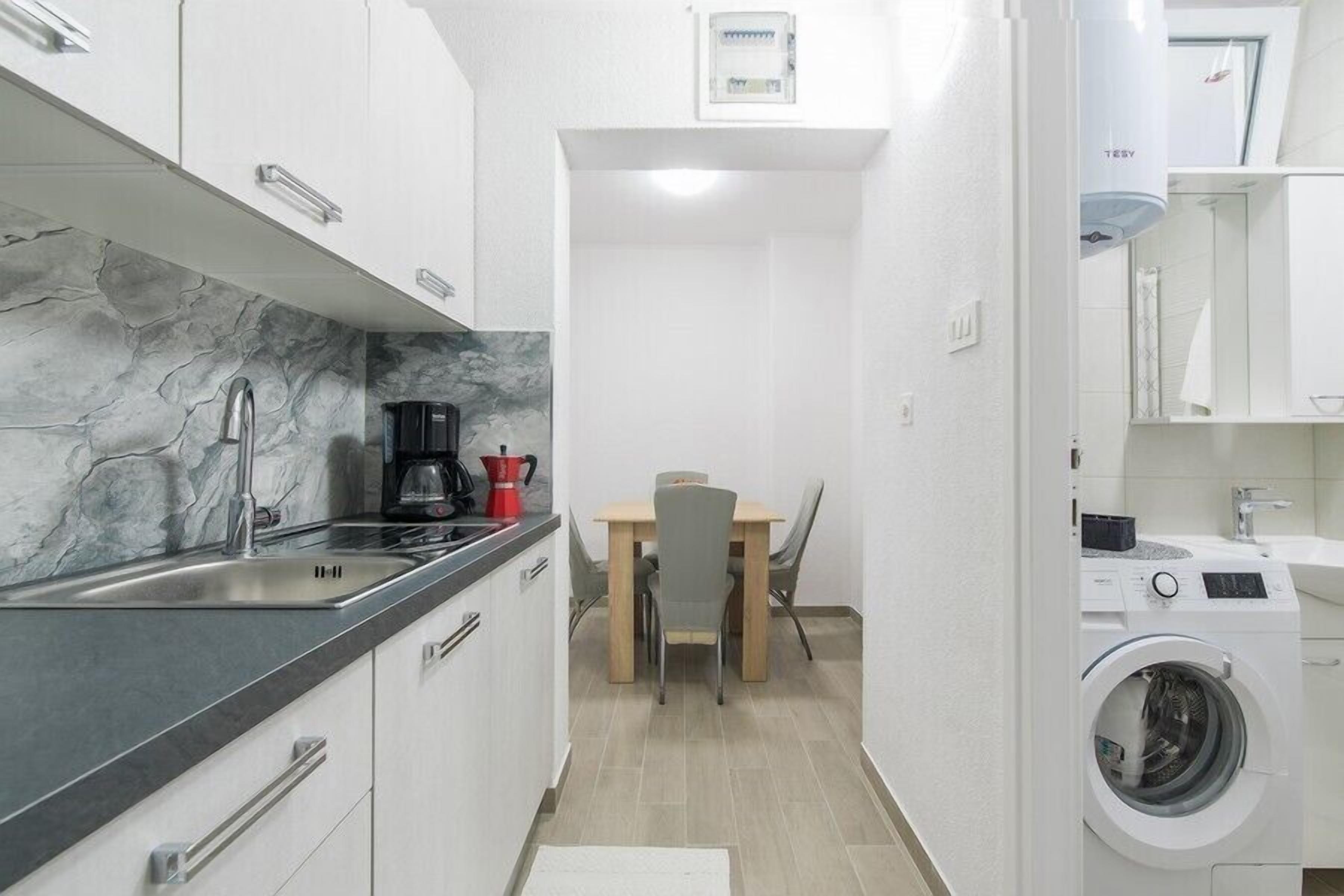 Een compacte keuken met een marmeren achterwand, een wastafel, een koffiezetapparaat en een eethoek met een tafel en stoelen.