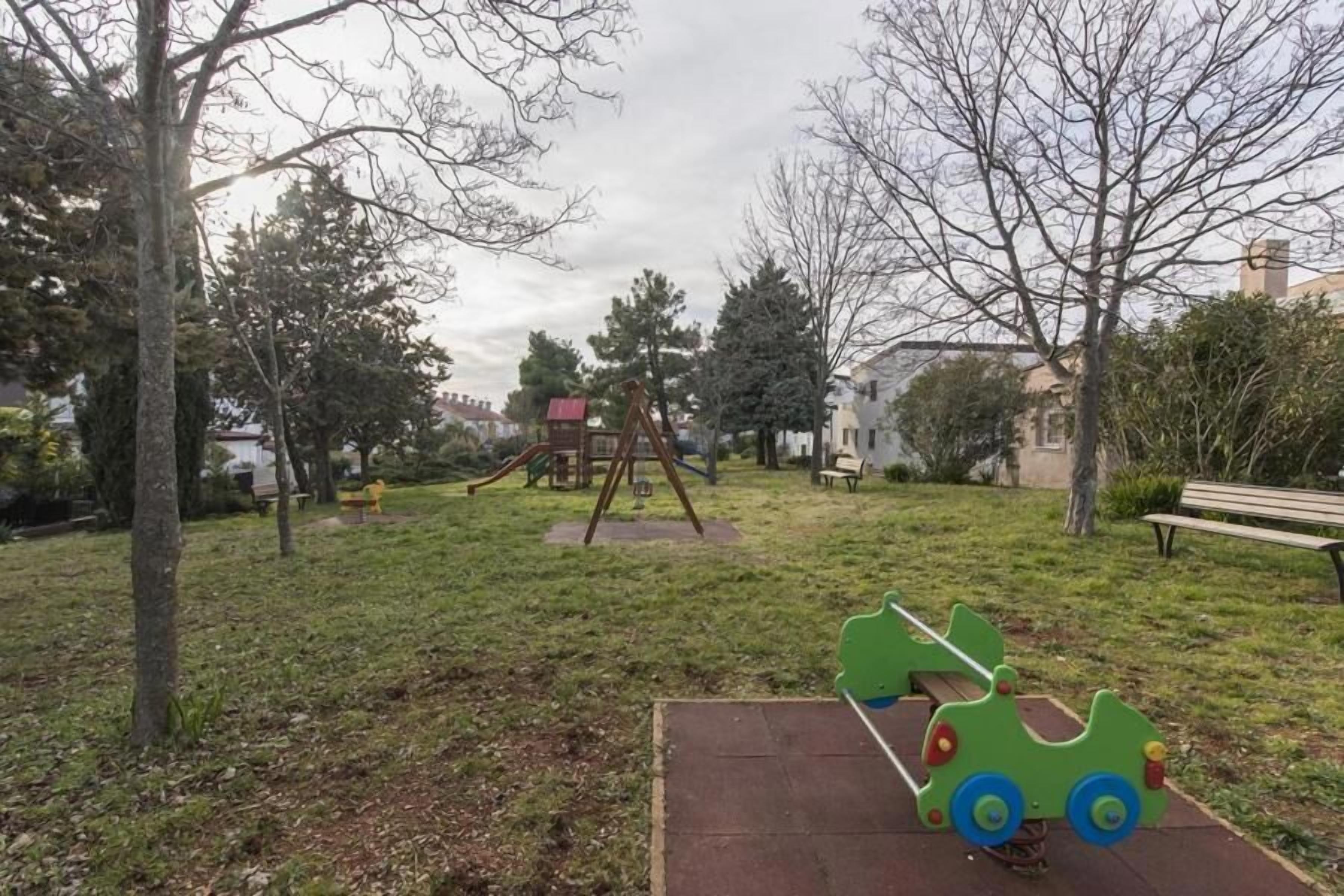 A playground with a swing set, a green toy car, and a bench.