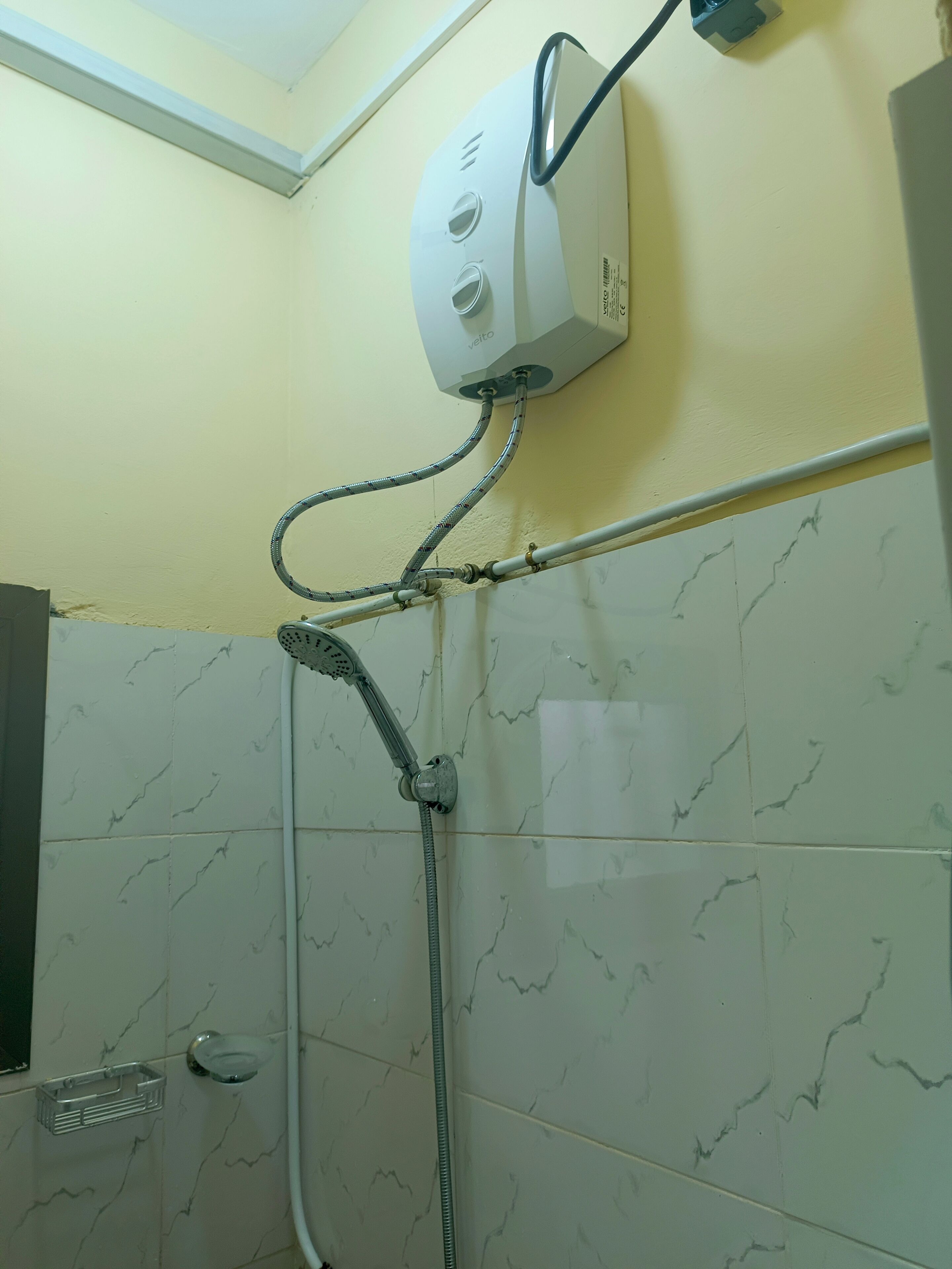 Ducha con cabezal de ducha manual, panel de control empotrado en la pared y pared revestida con azulejos de diseño marmolado.
