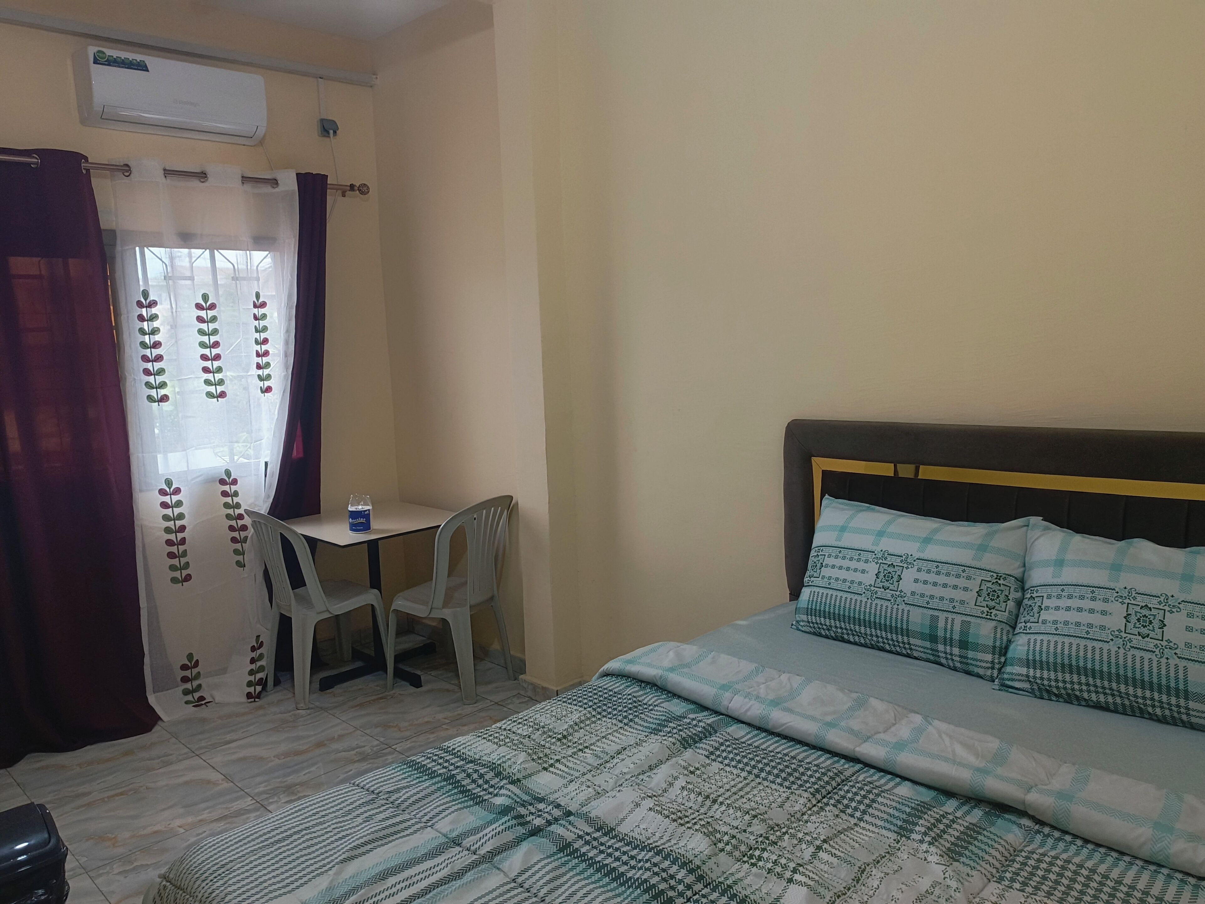 Una habitación con cama, escritorio, silla, aire acondicionado y ventana con cortinas.
