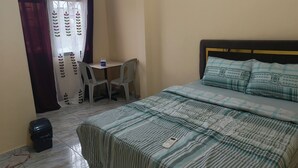 Ein Schlafzimmer mit Bett, kleinem Tisch, zwei Stühlen, einem Vorhang und einem Mülleimer.