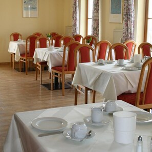 Un comedor con varias mesas y sillas, cada conjunto con manteles blancos y sillas acolchadas rojas.