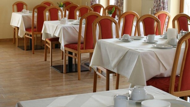 A dining area with tables set for service, chairs, and a window with curtains. - Apparthotel Garni Superior Simsseeblick (Bad Endorf)