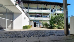 A hotel entrance with a paved courtyard, a balcony with railings, and a sign reading 'Appart-Hotel'. - Apparthotel Garni Superior Simsseeblick (Bad Endorf)