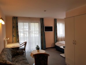 Ein Zimmer mit einer Couch, einem kleinen Tisch, einem Fernseher, einem Bett und einem Kleiderschrank.