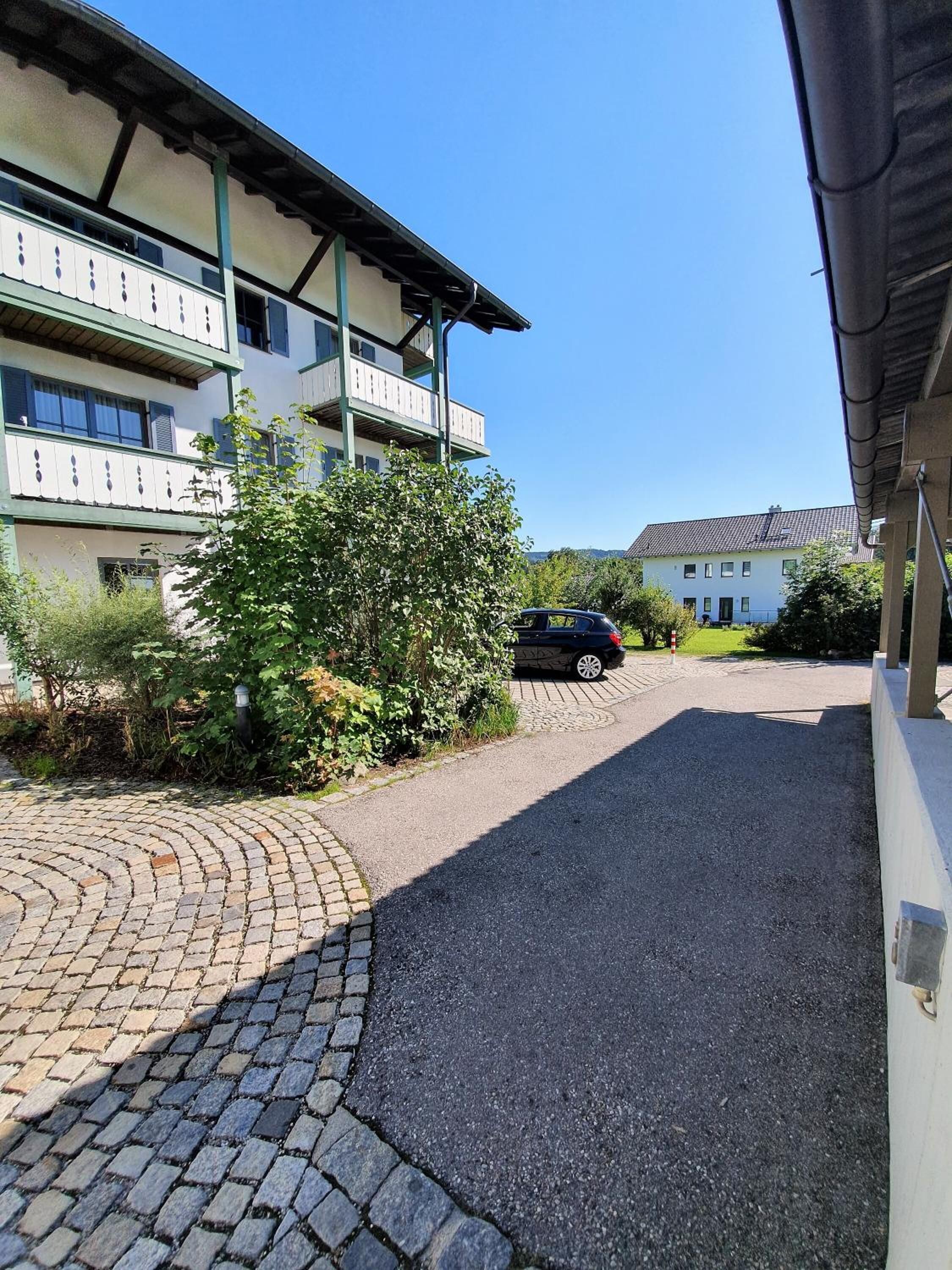 Een gebouw met een verharde oprit, een geparkeerde auto en een heldere lucht.