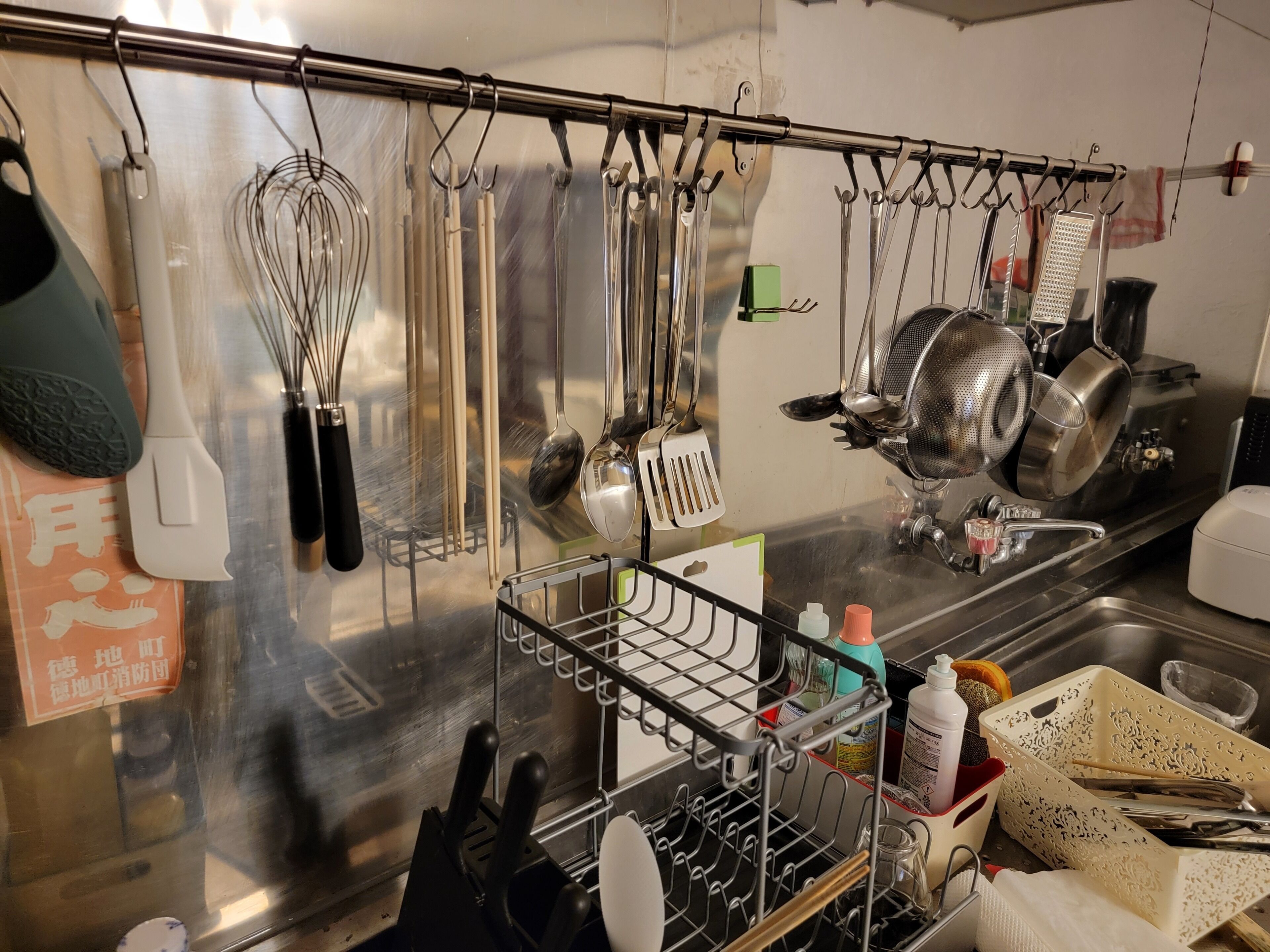 Une cuisine équipée d’appareils électroménagers en acier inoxydable, avec des ustensiles suspendus à un porte-ustensiles et un espace dédié à l’évier.