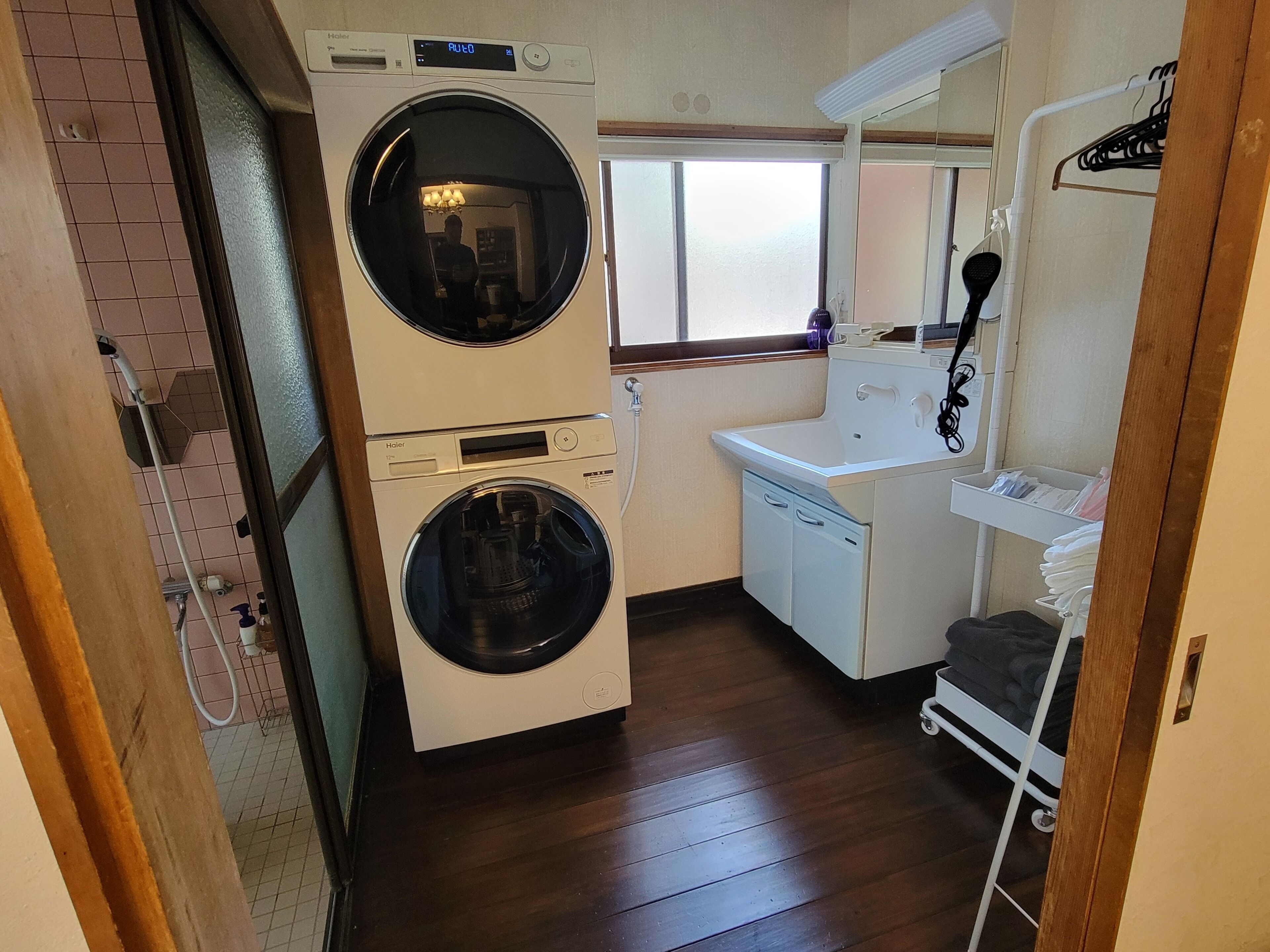 A compact laundry room with a front-loading washer and dryer, a small sink, and a drying rack.