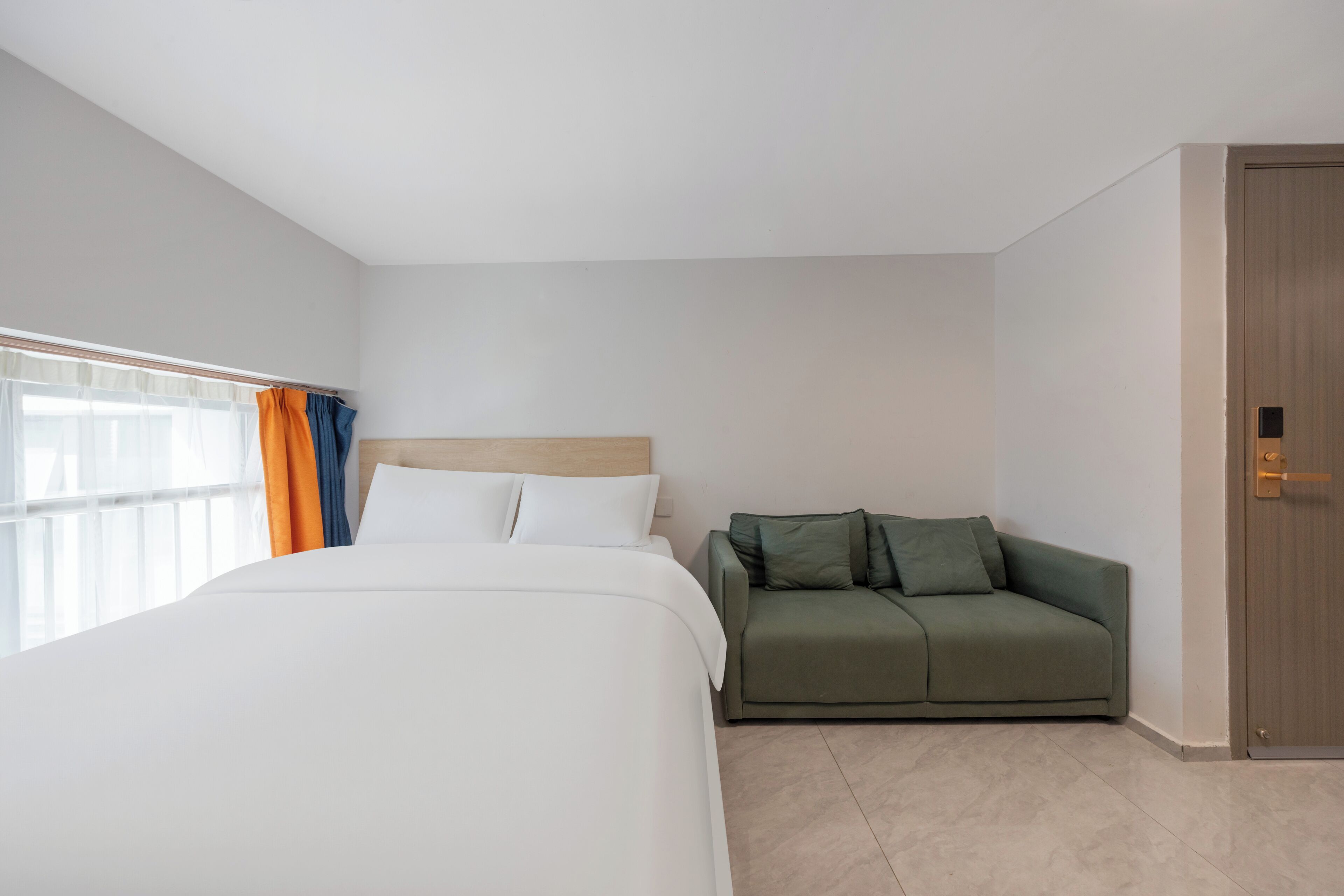 Ein Hotelzimmer mit einem Bett, einem grünen Sofa, einer Holztür und einem Fenster mit Vorhängen.
