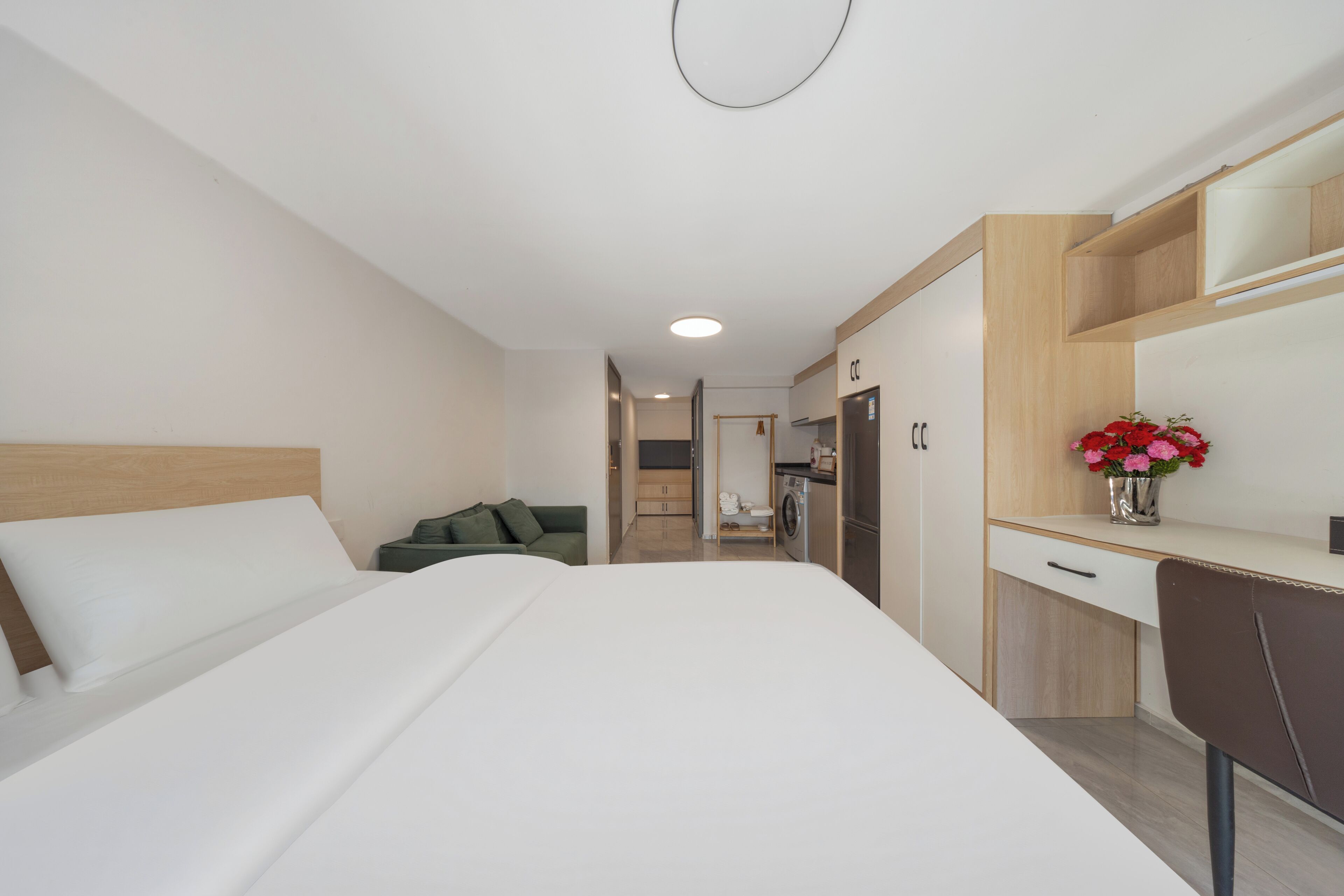Habitación de hotel con cama, escritorio, silla, una pequeña kitchenette y baño a la vista.