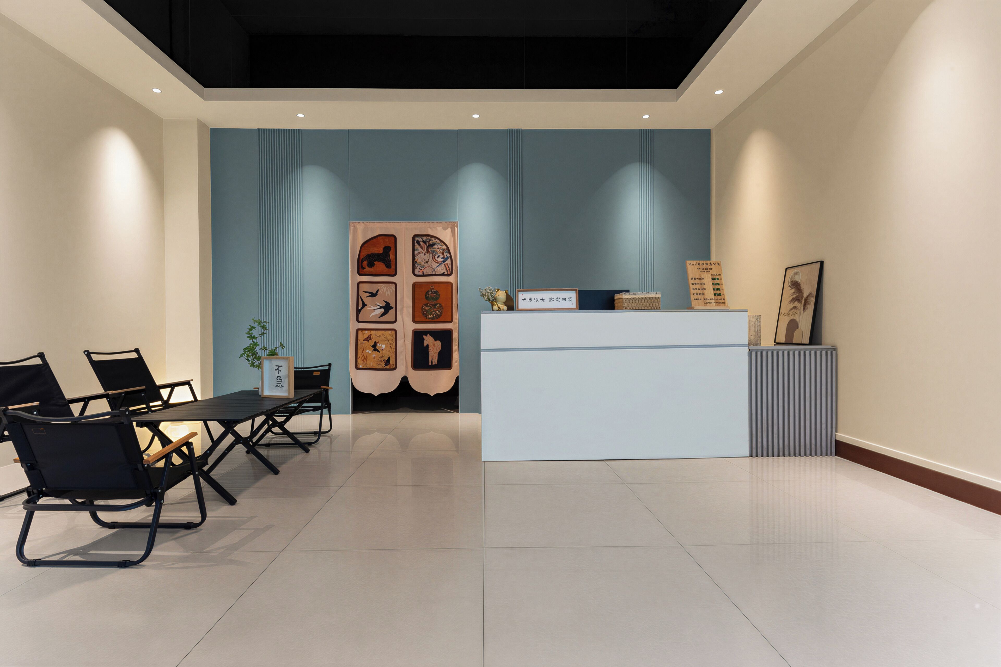 Un espace d’accueil avec un bureau blanc, des chaises noires et un mur orné de tableaux encadrés.