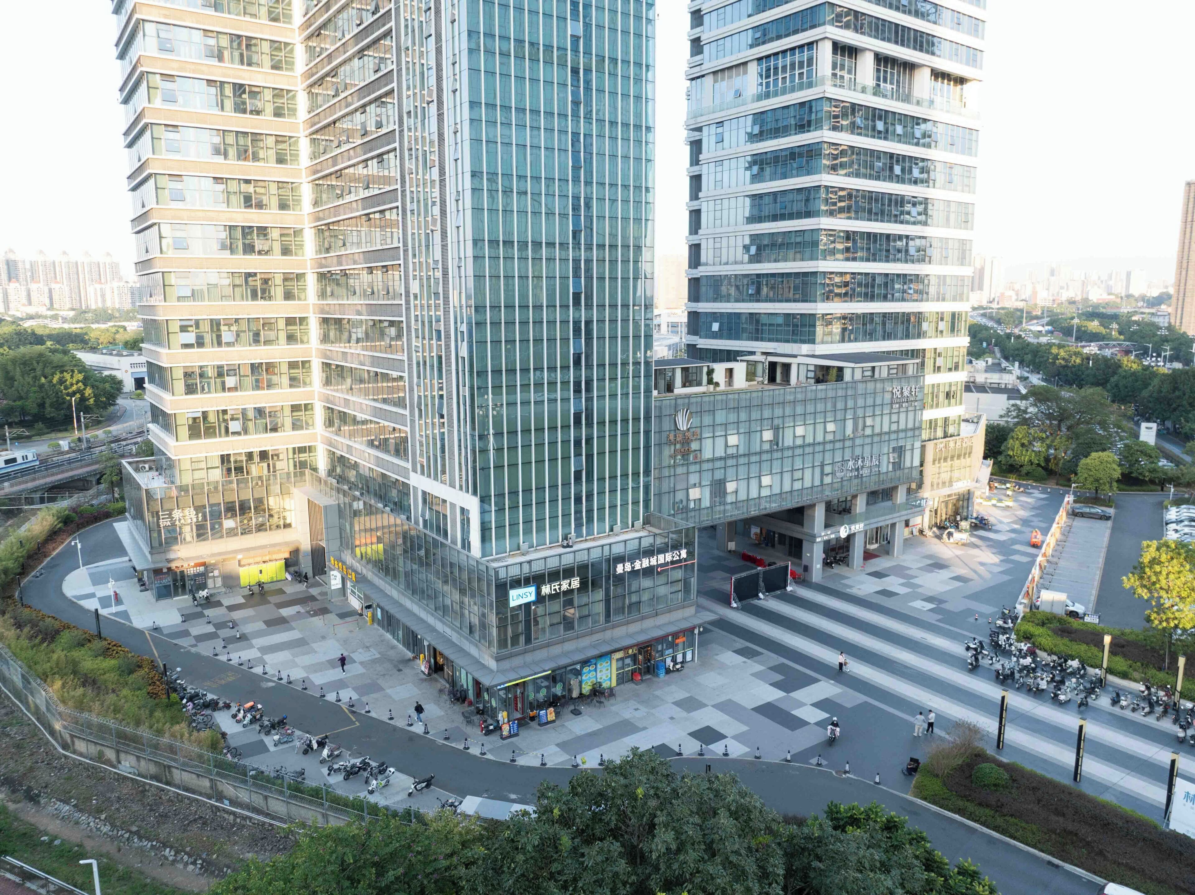 A modern building with multiple floors, large glass windows, and a commercial ground floor with shops and outdoor seating.