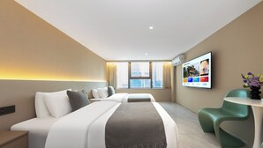 Ein Hotelzimmer mit einem großen Bett, einem Schreibtisch, einem Stuhl, einem Fernseher und einem Fenster mit Blick auf die Stadt.