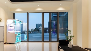Eine moderne Hotelhalle mit einem Verkaufsautomaten, einer Sitzecke und großen Fenstern mit Blick auf die Stadt.