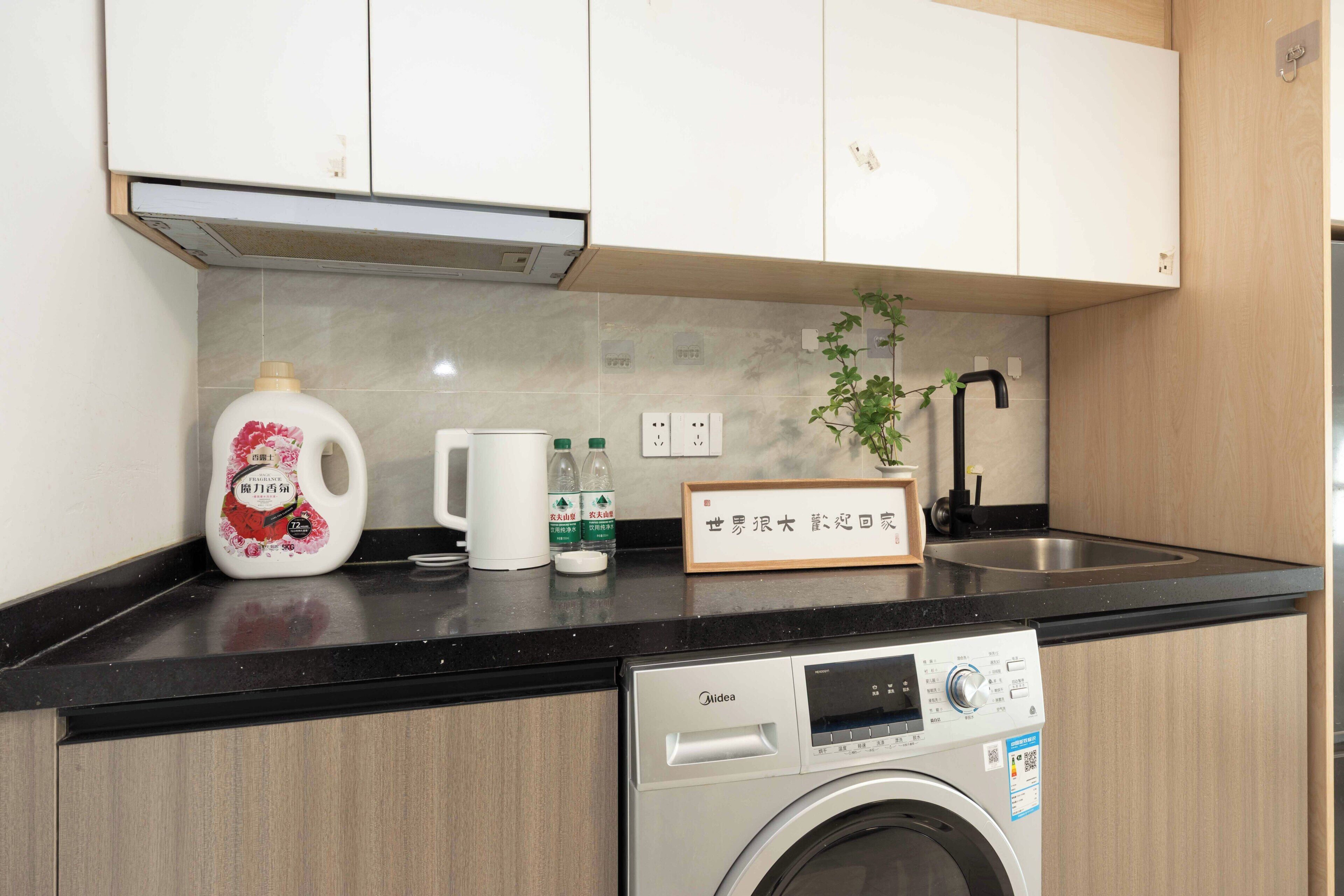 Una cocina con lavadora, un lavabo y una encimera con diversos objetos.