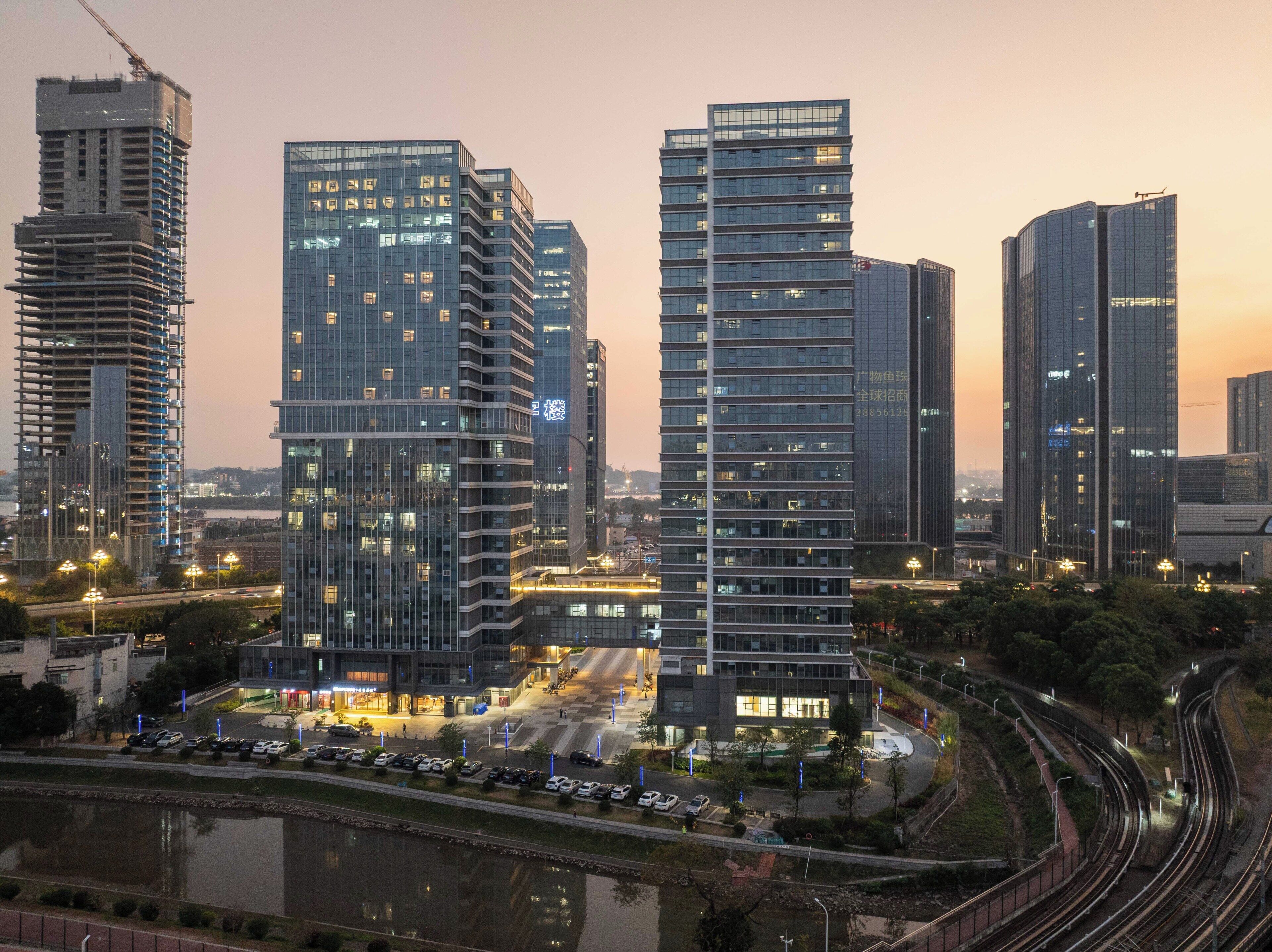 A modern urban skyline with high-rise buildings, a river, and a curved railway track.