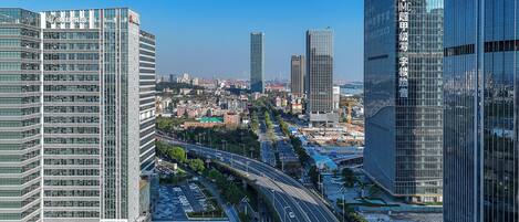 A cityscape with modern high-rise buildings, a multi-lane road, and a clear blue sky.