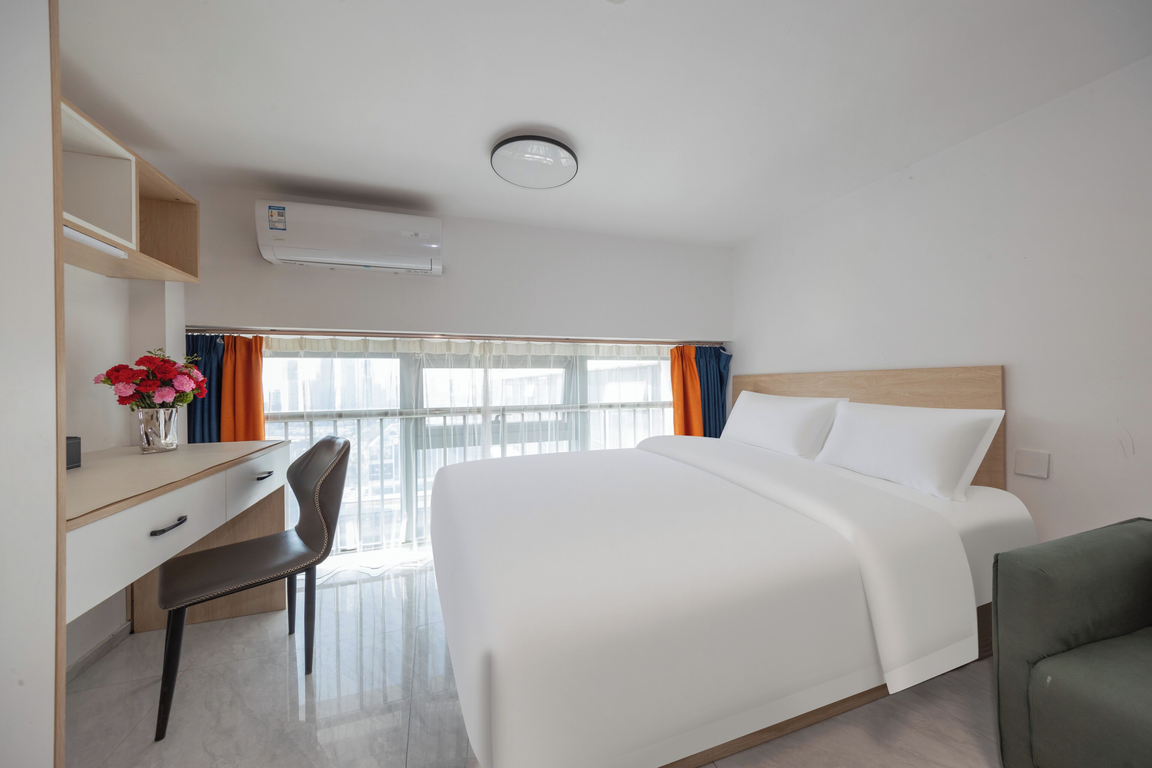 Una habitación de hotel con cama, escritorio, silla y ventana con cortinas.