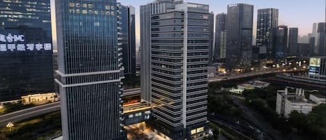 A high-rise building with a modern glass facade, surrounded by other tall buildings, and a busy road with moving vehicles.
