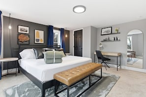 A modern bedroom with a bed, bench, desk, and chair, featuring artwork and a mirror. - NEW Spacious and fun packed large home in Baltimore County (Reisterstown)