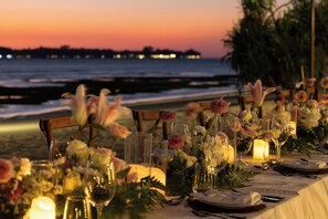 A table set for a meal with candles, flowers, and glasses, overlooking a beach at sunset. - The Sira, a Luxury Collection Resort & Spa, Lombok (Tanjung)