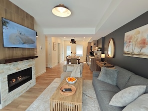Ein modernes Wohnzimmer mit Kamin, Flachbildfernseher, einer Couch, einem Couchtisch und einem Essbereich im Hintergrund.